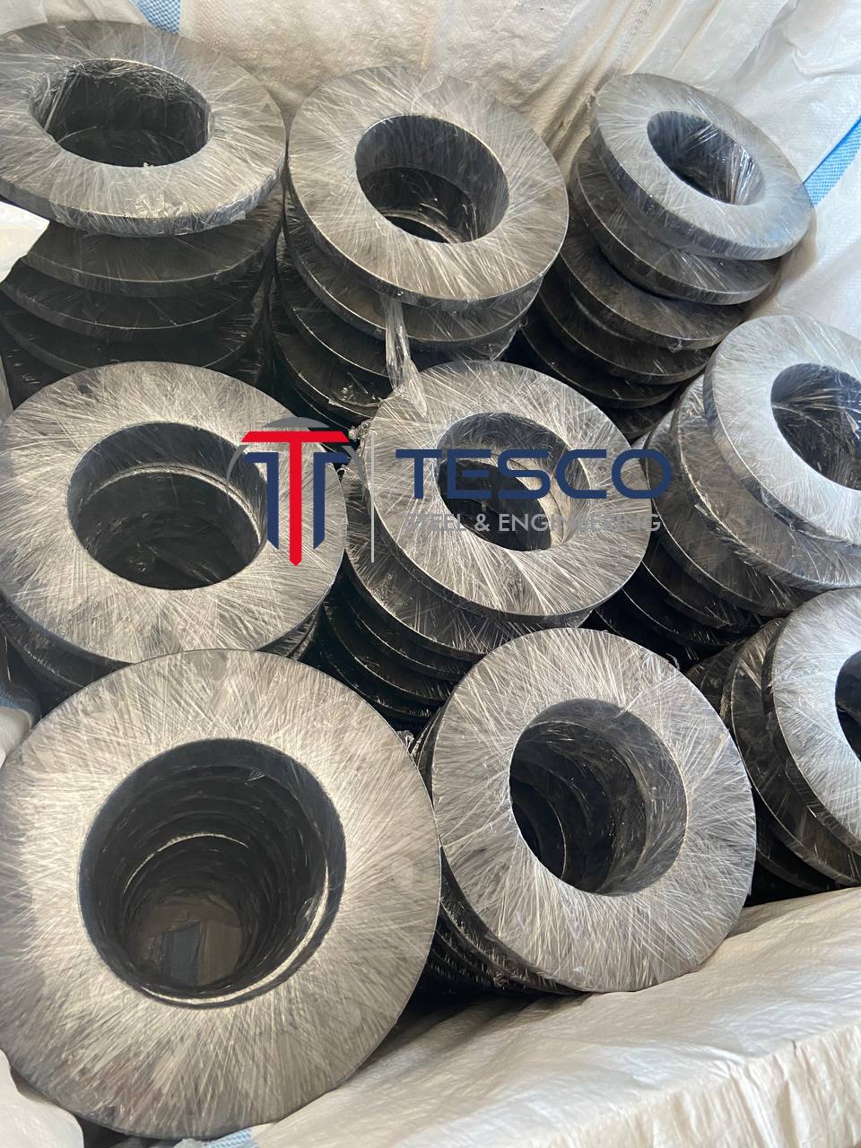Close-up of ASTM A105 carbon steel weld neck flanges individually plastic-wrapped showing bore detail — WNRF carbon steel flanges export packaging Tesco Steel India