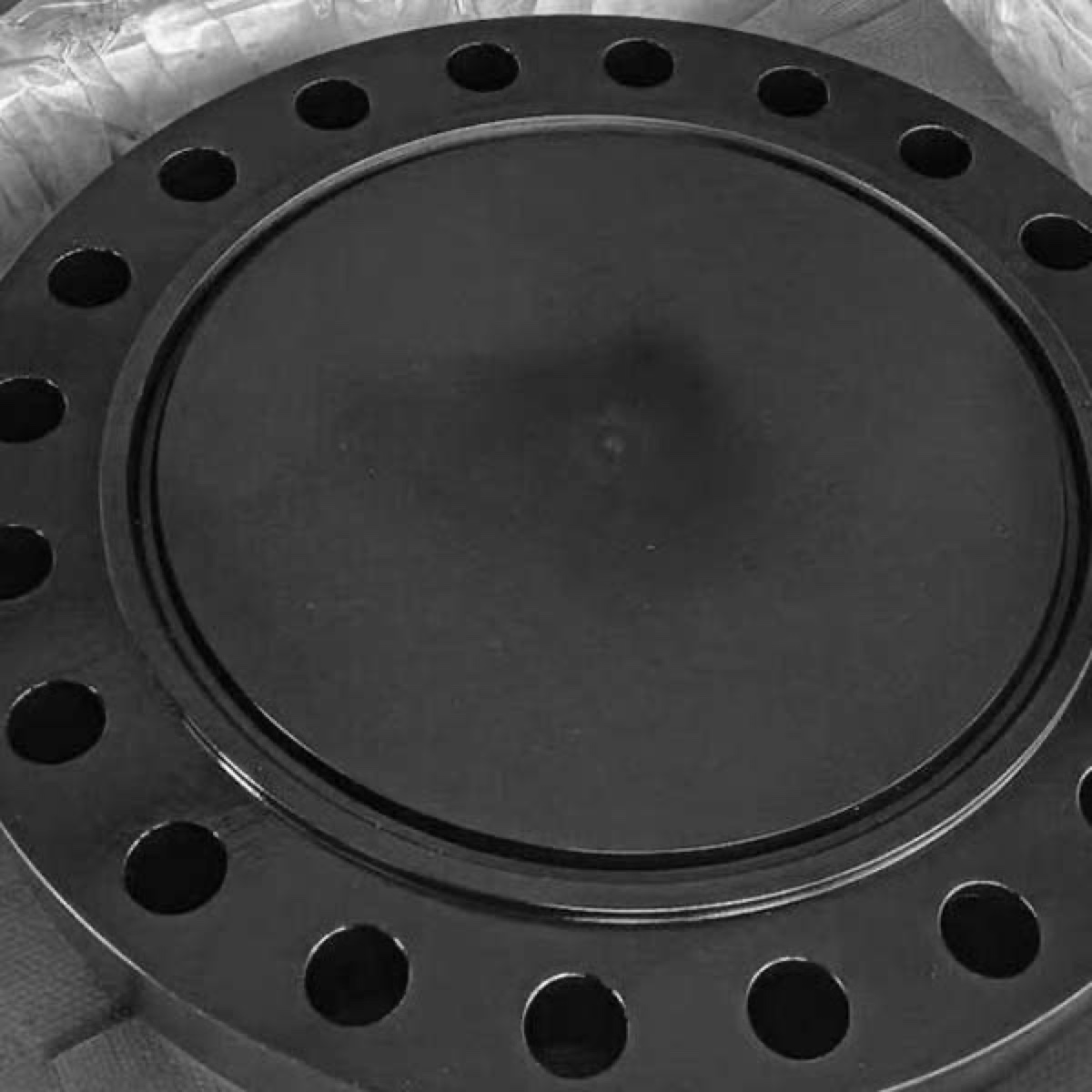 Black coated raised face blind flange closeup showing bolt holes and machined facing