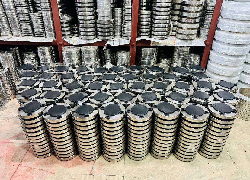 Large bulk stock of duplex steel blind flanges with plastic face-protection caps stacked before dispatch — ASTM A182 F51 F60 S31803 S32205, Tesco Steel & Engineering