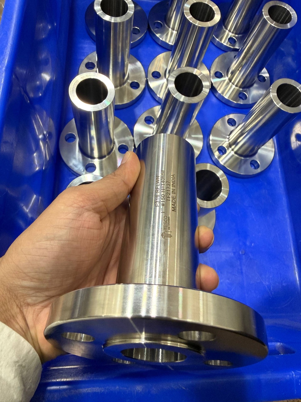 F316 long weld neck flange 1 inch 150 class held in hand over a bin of finished LWN flanges at Tesco works