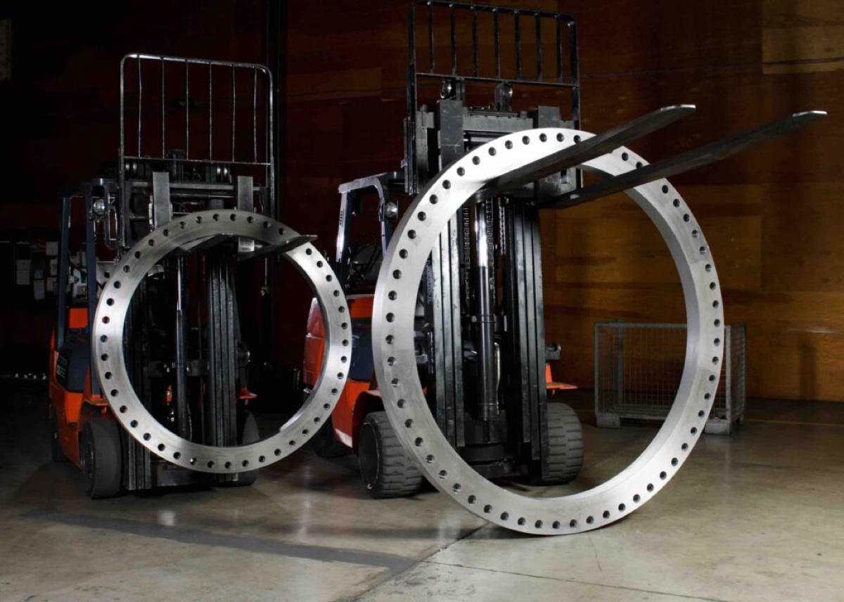 Two giant large diameter drilled flanges being handled on forklifts in the flange works