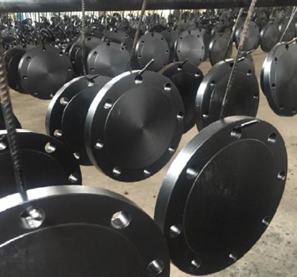 Black coated forged blind flanges hanging on the coating and finishing line at the works