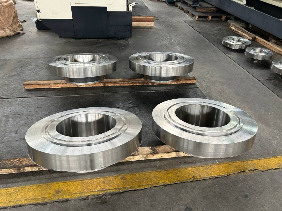 Machined flanges with ring grooves stacked on wooden battens beside the CNC machining centre
