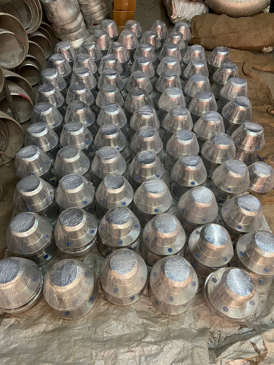 Hundreds of stainless steel weld neck flanges plastic-wrapped and laid out in warehouse before bulk export packing — Tesco Steel & Engineering India